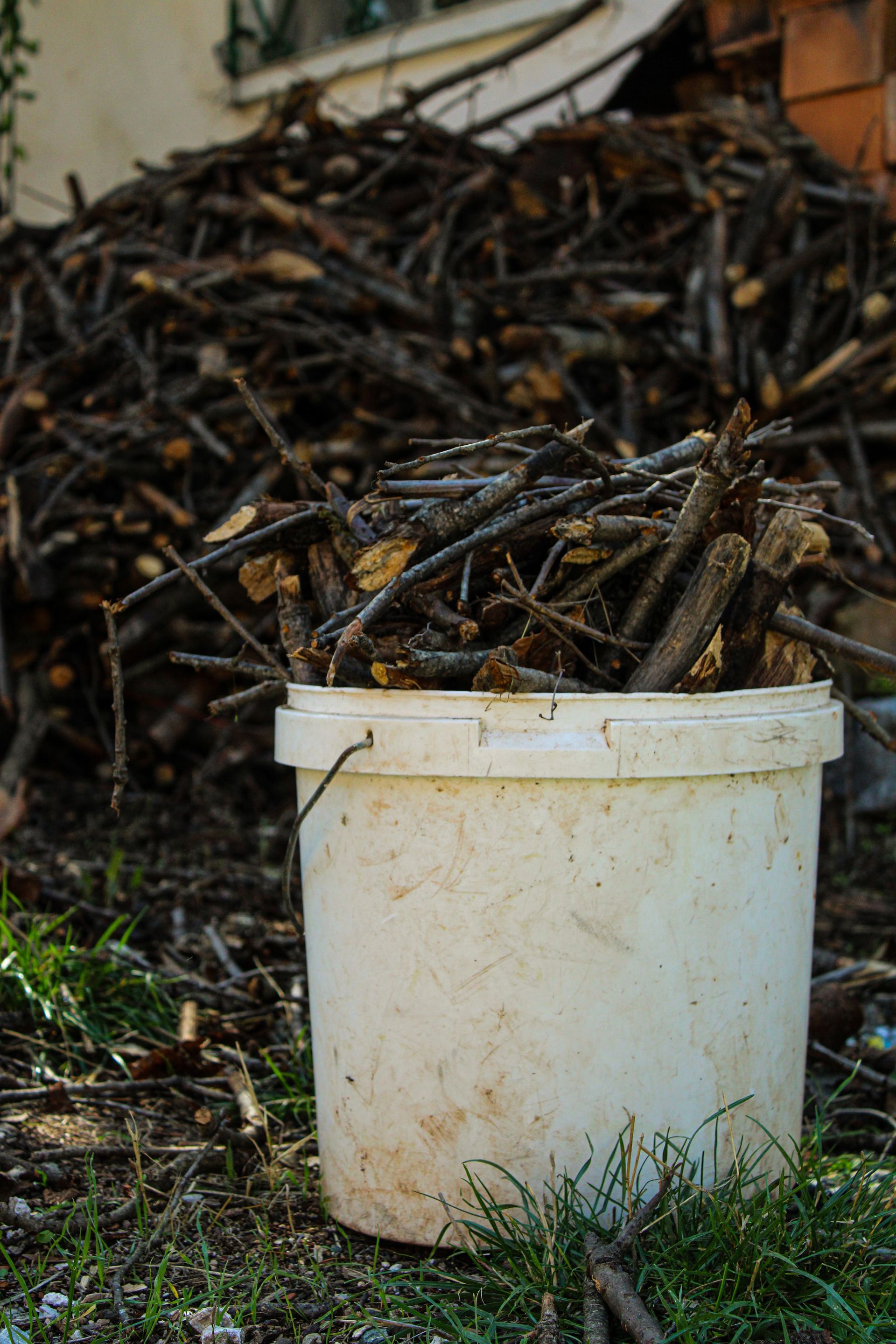 A white bucket filled with firewood sticks against a rural scene in Çorum, Turkey.